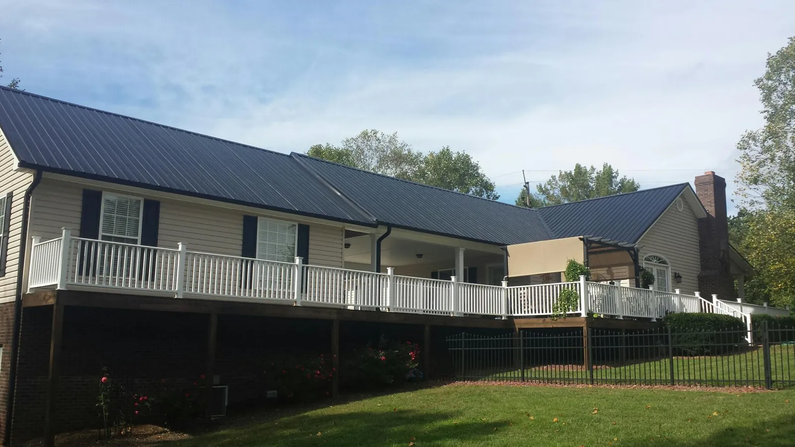 Black metal roof above a long white railed deck on a hillside home in Greenwood