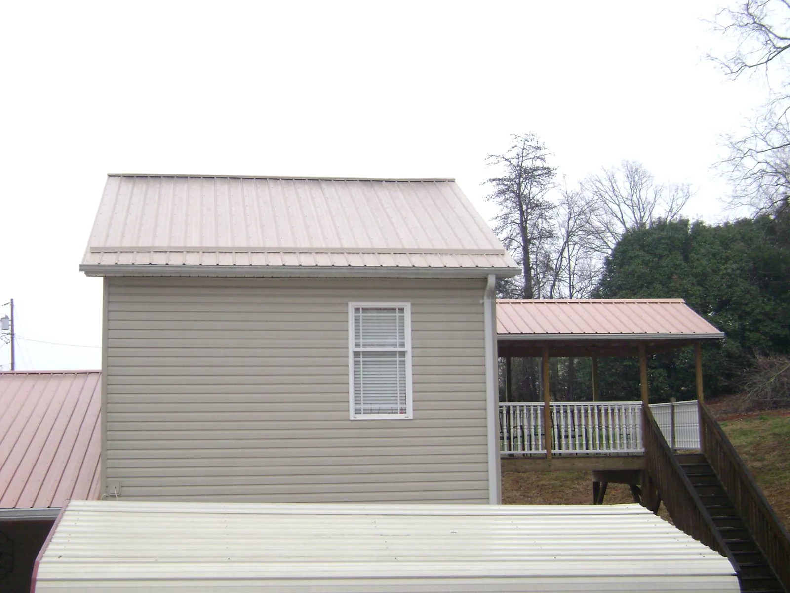 Tan metal roofs on a two story addition and attached porch, from a Roof Replacement job in Greenwood
